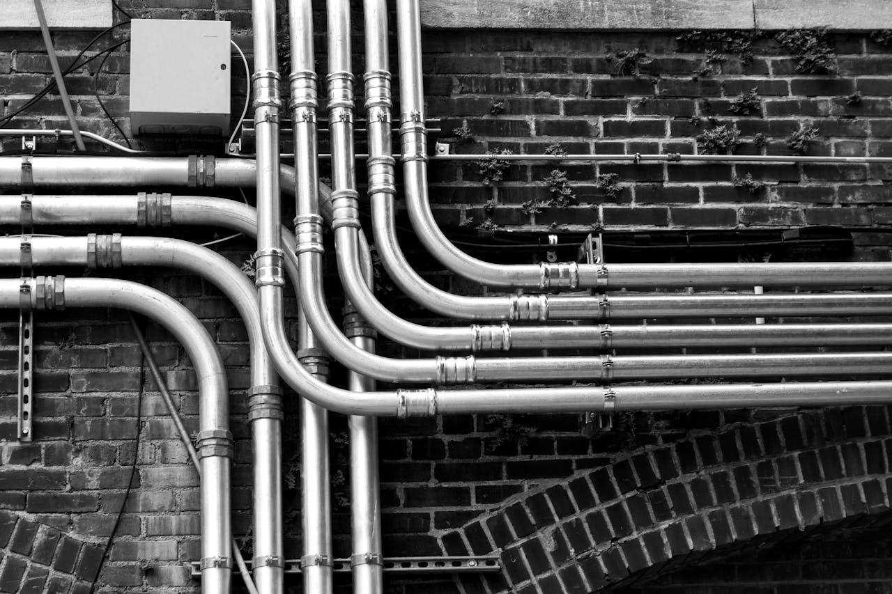 Services Black and white image of industrial stainless steel pipes mounted on a brick wall.