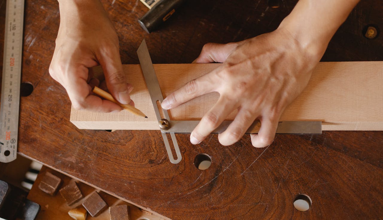 High angle of skilled man using bevel tool and pencil while measuring angle of cut on workshop